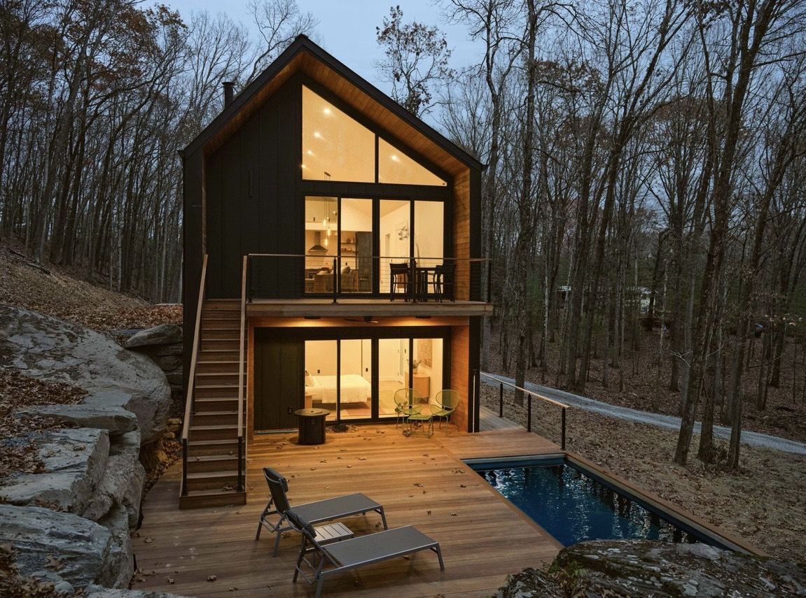 Oak Ridge, a two-story black-clad home glowing at dusk with a pool and deck in the Catskills woods