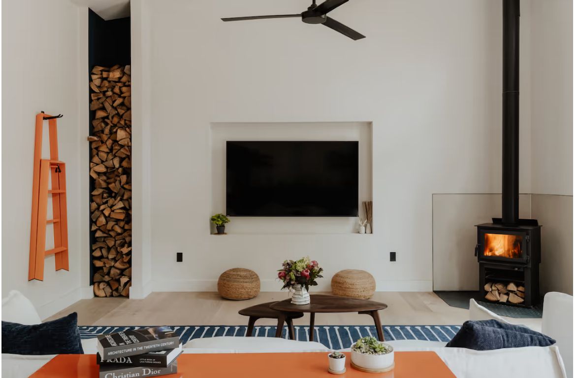 Living room at White Pines with a wood-burning stove, stacked firewood, and a low sofa